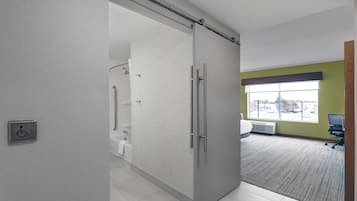 A modern hotel room with a sliding door to a bathroom, a large window with a view, and a carpeted floor.