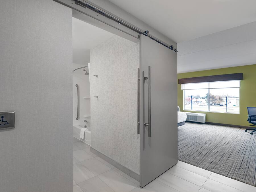 A modern hotel room with a sliding door to a bathroom, a large window with a view, and a carpeted floor.