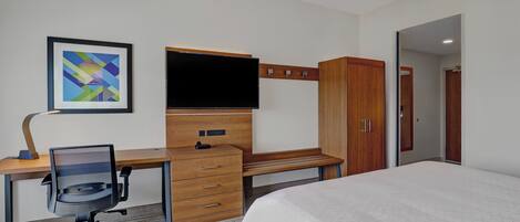Une chambre d’hôtel comprenant un lit, un bureau avec une chaise, une télévision, une armoire et un tableau encadré au mur.