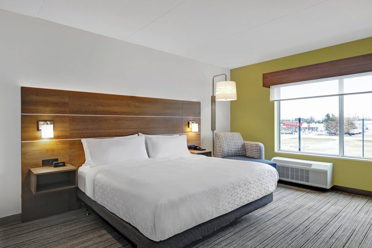 Une chambre d’hôtel avec un grand lit, des lampes de chevet, une chaise, une fenêtre donnant sur un beau paysage et un radiateur.