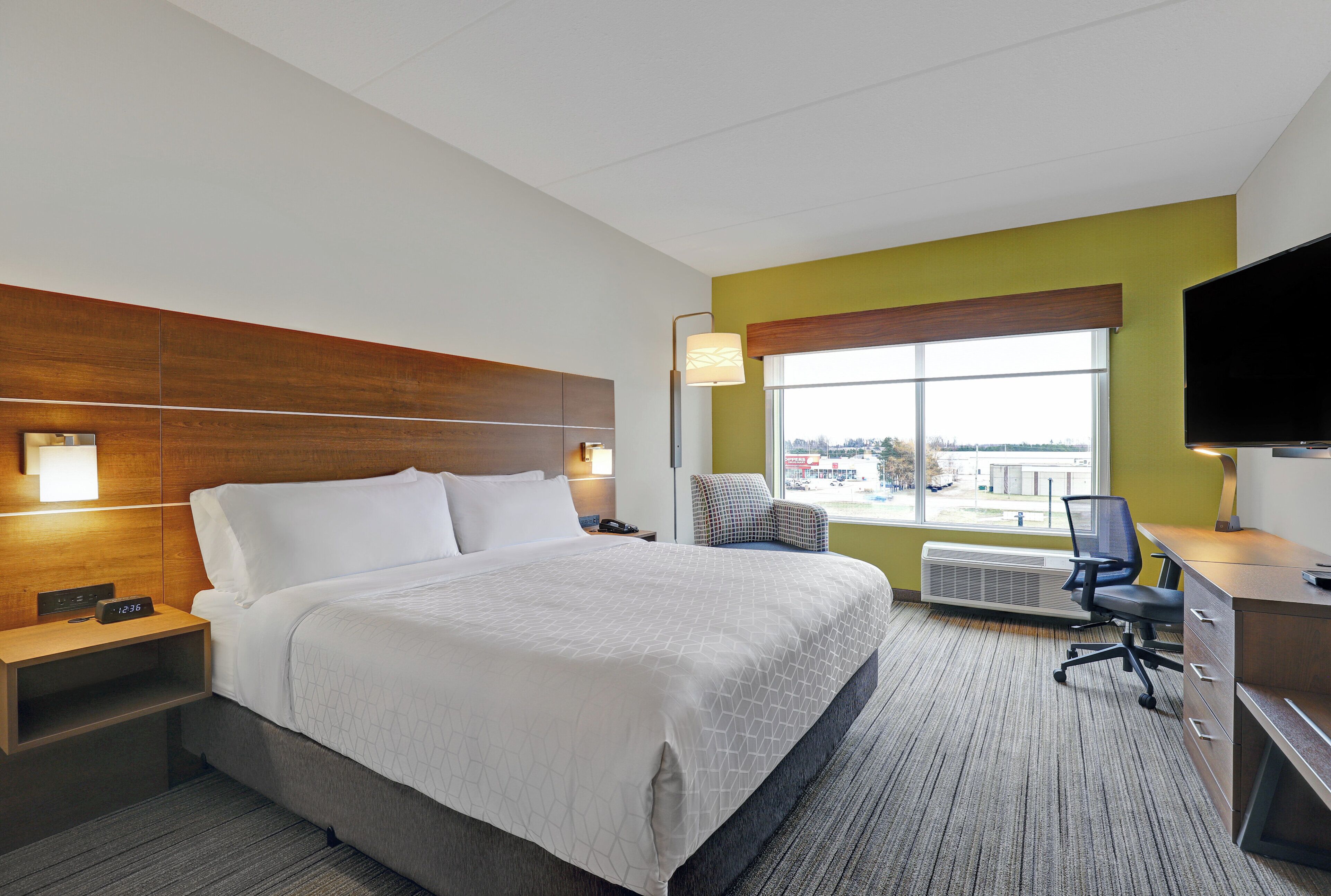 Habitación de hotel con cama, mesitas de noche, escritorio, silla, televisor y ventana con vistas al exterior.