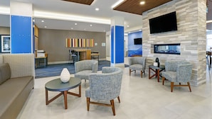 A modern lobby with a blue and grey color scheme, featuring a seating area with sofas and armchairs, a flat-screen TV mounted on a stone wall, and a reception desk in the background. - Holiday Inn Express & Suites Port Elgin by IHG (Saugeen Shores)