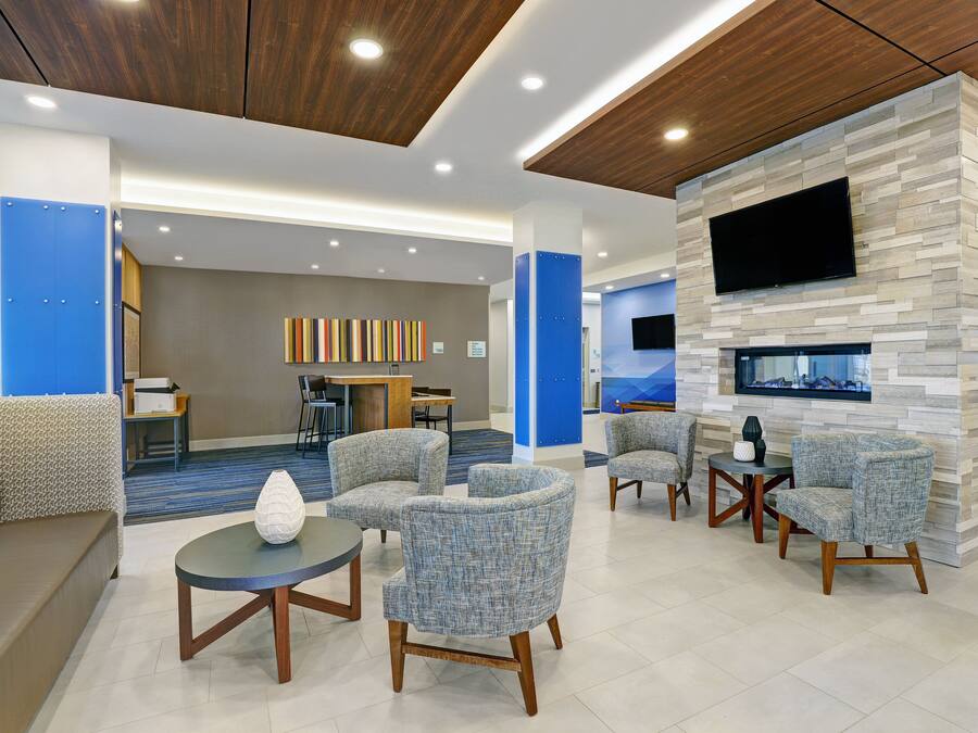 A modern lobby with a blue and grey color scheme, featuring a seating area with sofas and armchairs, a flat-screen TV mounted on a stone wall, and a reception desk in the background.