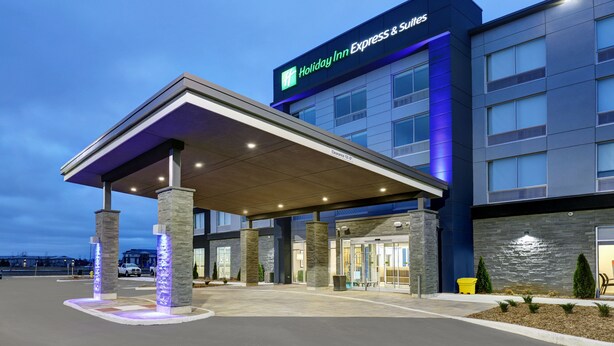 A Holiday Inn Express & Suites building with a covered entrance, stone pillars, and a blue-lit facade. - Holiday Inn Express & Suites Port Elgin by IHG (Saugeen Shores)