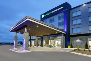 A Holiday Inn Express & Suites building with a covered entrance, stone pillars, and a blue-lit facade. - Holiday Inn Express & Suites Port Elgin by IHG (Saugeen Shores)