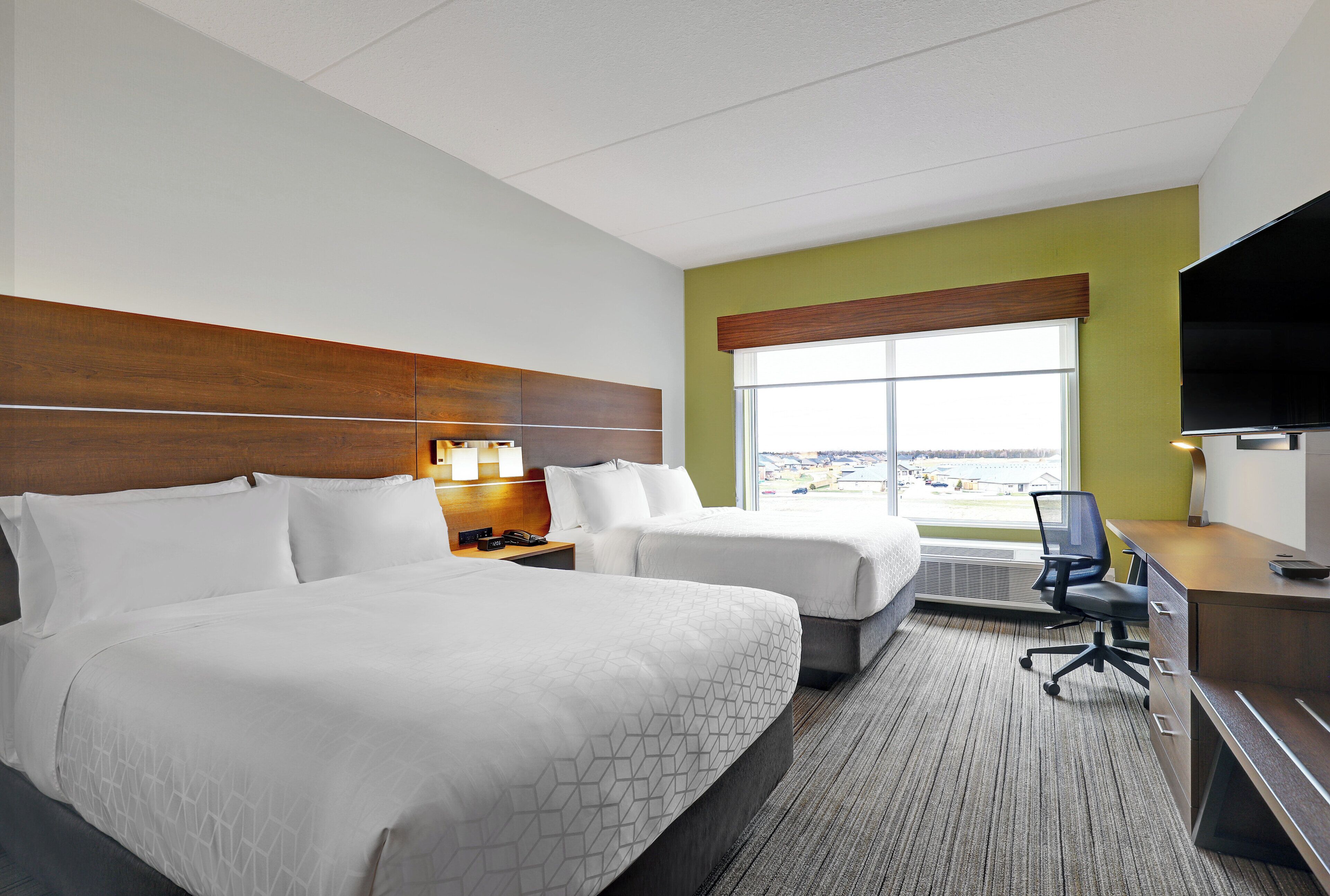 A hotel room with two beds, a desk, a TV, and a window with a view.