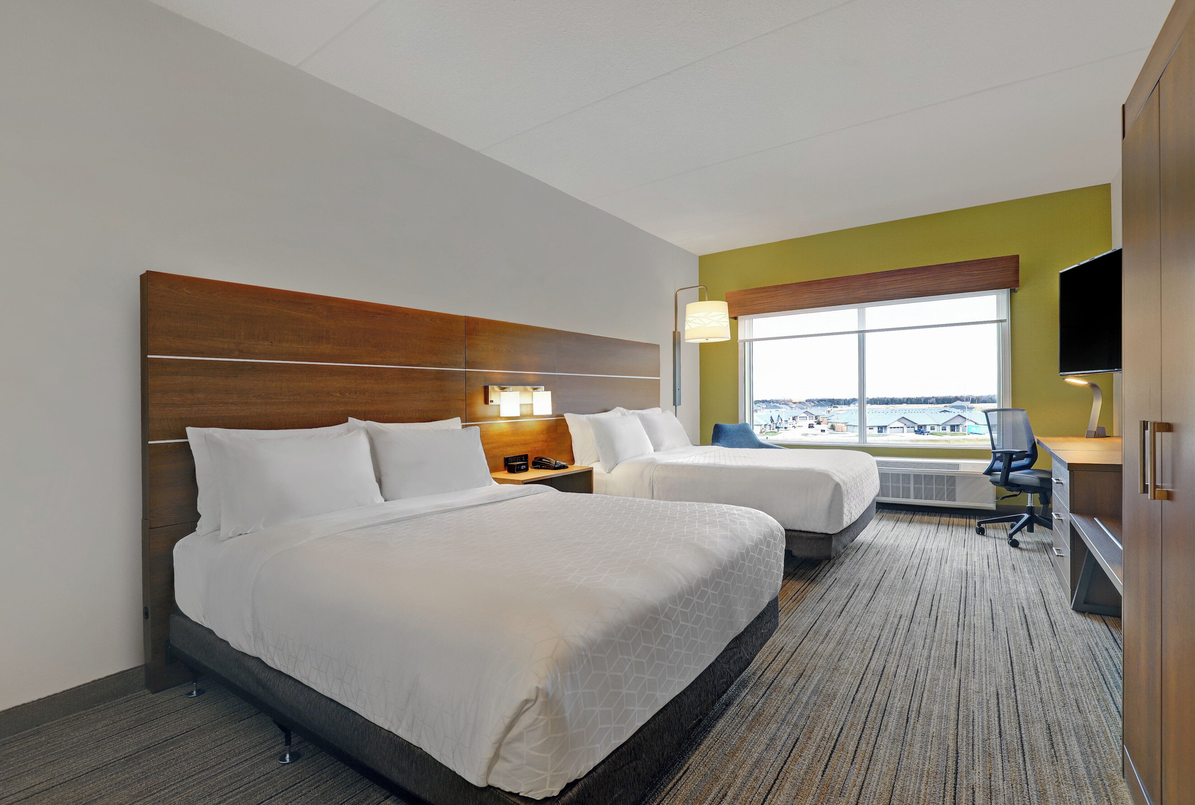 A hotel room with two beds, a desk, a chair, a TV, and a window with a view.