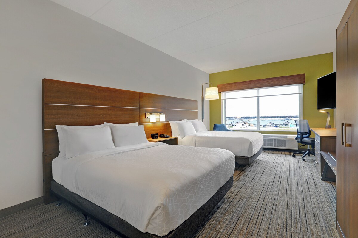 A hotel room with two beds, a desk, a chair, a TV, and a window with a view.
