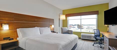 A hotel room with a bed, a desk, a chair, a TV, and a window with a view.