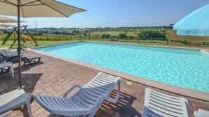 Une piscine à l’eau d’un bleu cristallin, entourée d’une terrasse en briques. On y trouve des chaises longues blanches et une balançoire.