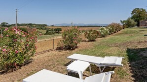 Un jardin avec des chaises longues blanches, un bâtiment en pierre et une vue dégagée sur la campagne.
