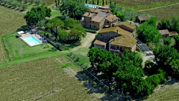 Vue aérienne d’une propriété rurale comprenant plusieurs bâtiments, une piscine et des champs agricoles environnants.