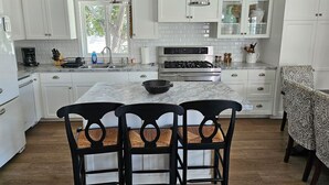 A modern kitchen with white cabinets, a marble countertop, a gas stove, and black chairs.