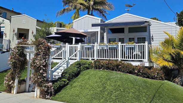 A residential house with a white fence, a covered patio, and a palm tree.