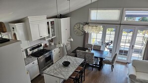 A modern kitchen with white cabinets, a marble countertop, and a dining area with patterned chairs and a chandelier.