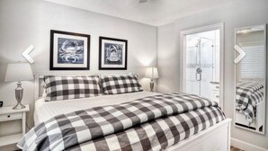 A bedroom with a bed, two bedside lamps, a ceiling fan, and two framed artworks on the wall.
