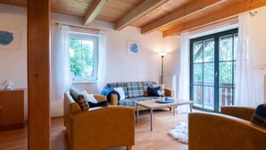A cozy living room with a sofa, two armchairs, a coffee table, and a lamp. There are large windows with curtains, a wooden ceiling, and a door on the left. - Holiday Hill 33 by Interhome (Cerny Dul/Cista)