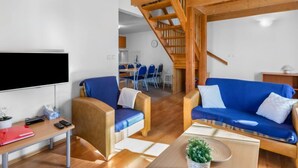 A modern living room with a wooden ceiling, a flat-screen TV, two blue sofas, a wooden coffee table, and a staircase leading to an upper level. - Holiday Hill 33 by Interhome (Cerny Dul/Cista)