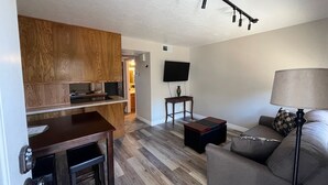 Ein modernes Wohnzimmer mit einer Holzwand, einem Flachbildfernseher, einer Couch, einem Couchtisch und einer Lampe.