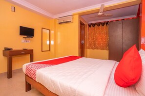 A hotel room with a bed, a TV, a wardrobe, and an air conditioning unit.