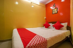 A hotel room with a bed, red and white bedding, and a red wall.