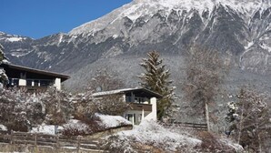 A mountain lodge with a modern design, featuring a large windowed room and a view of snow-covered peaks.