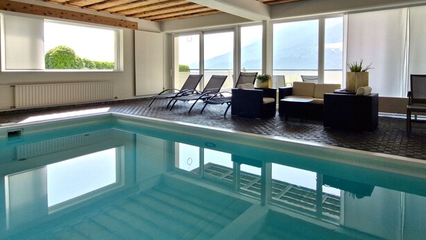 An indoor swimming pool with lounge chairs and a view of mountains.