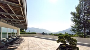 A terrace with sun loungers, a stone planter with a bonsai tree, and a view of mountains.