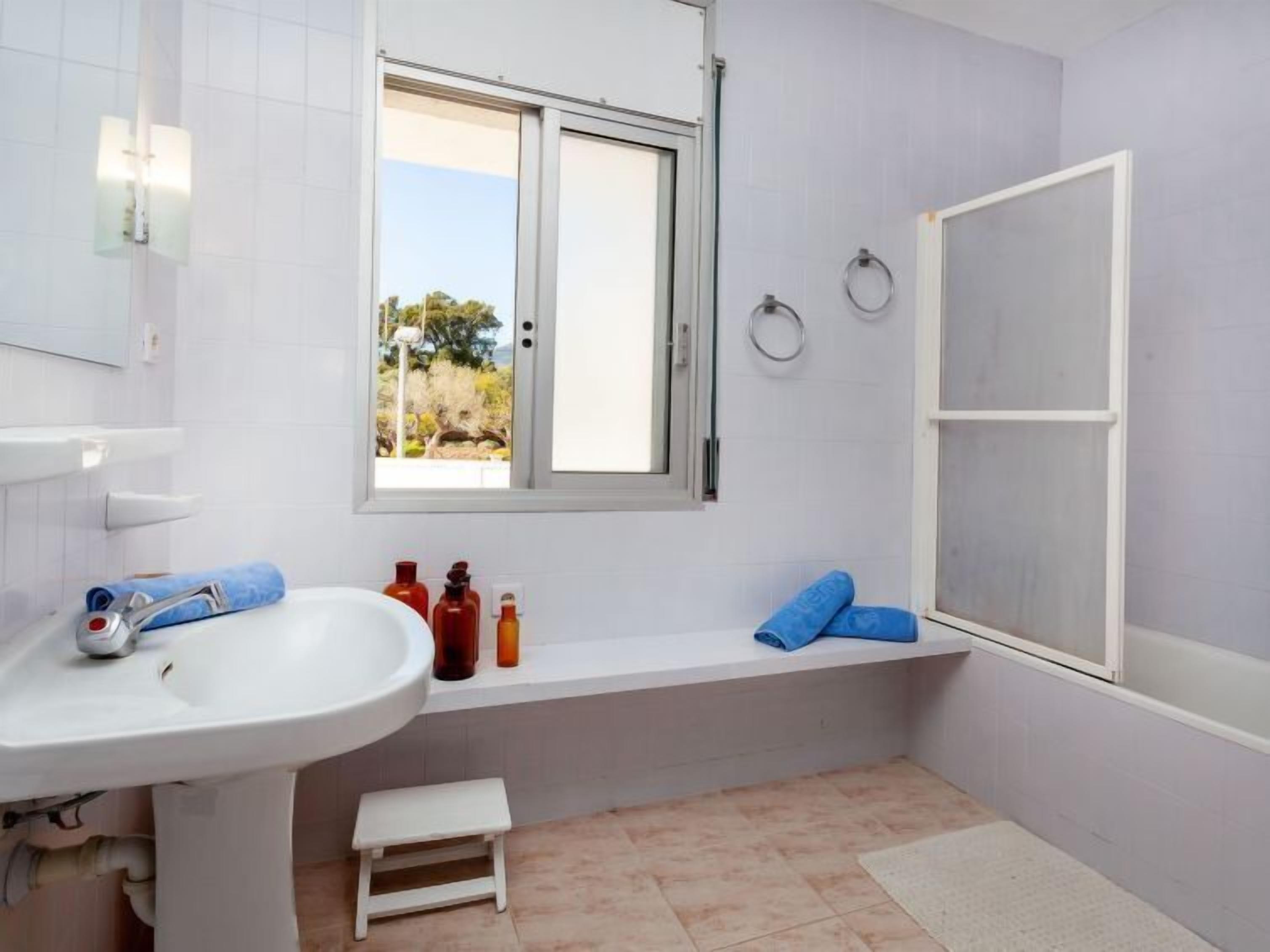 Ein Badezimmer mit einem weißen Waschbecken, einem Fenster, einer Badewanne und einer kleinen Stufe zum Einstieg in die Badewanne.