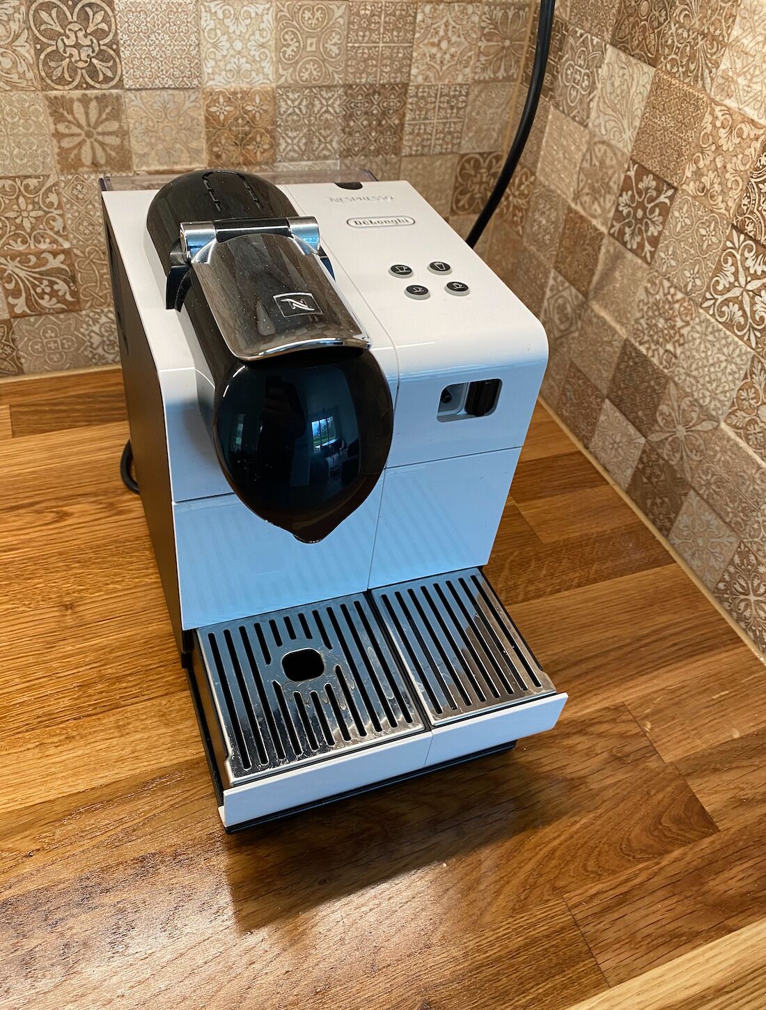 Une machine à café dotée d’un bac d’égouttement noir et d’un panneau de commande, le tout posé sur une surface en bois.