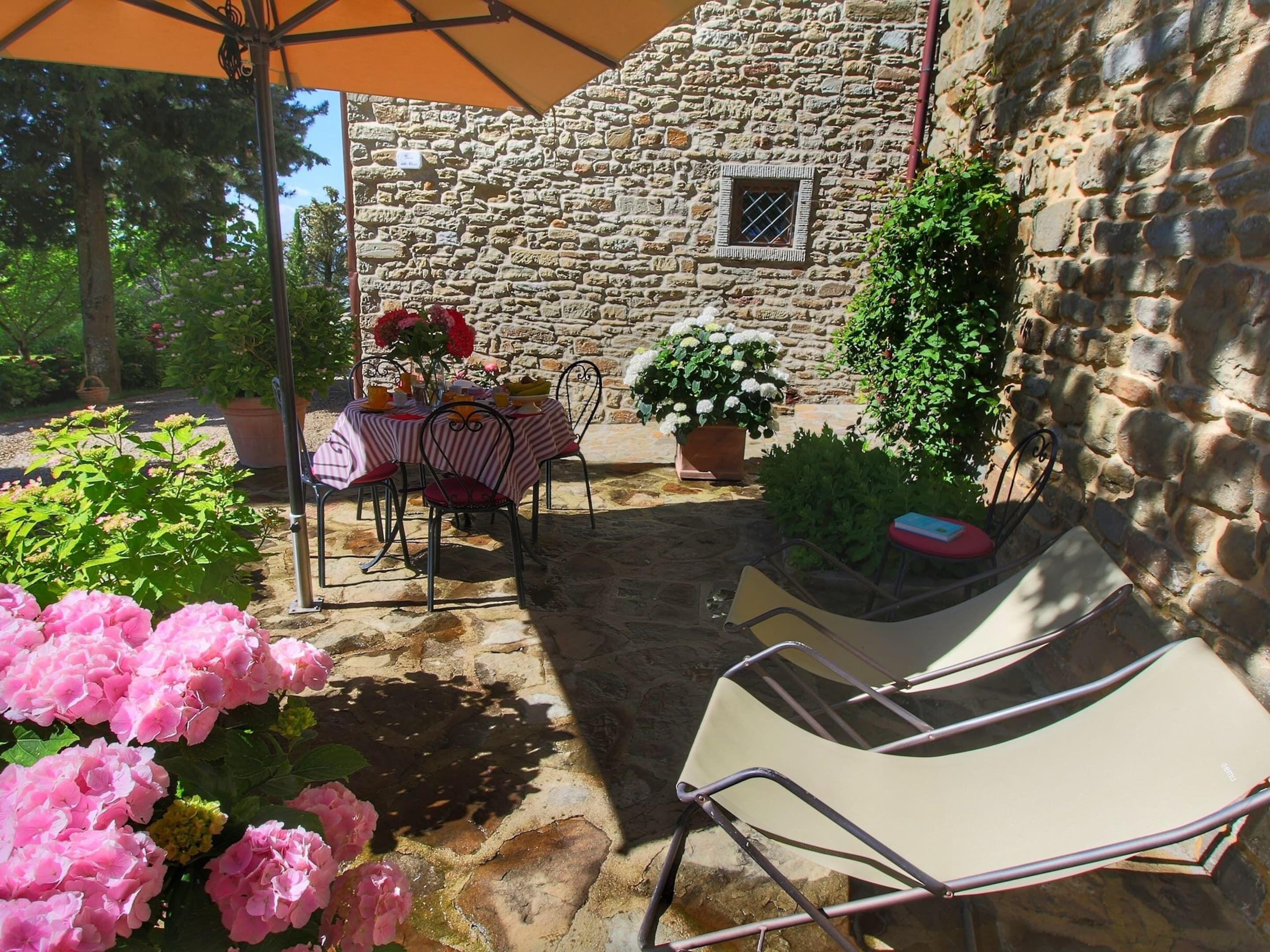 An outdoor patio with stone walls, a table set for dining, and potted plants.