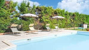 Una piscina con sillones de descanso y sombrillas, rodeada de vegetación.