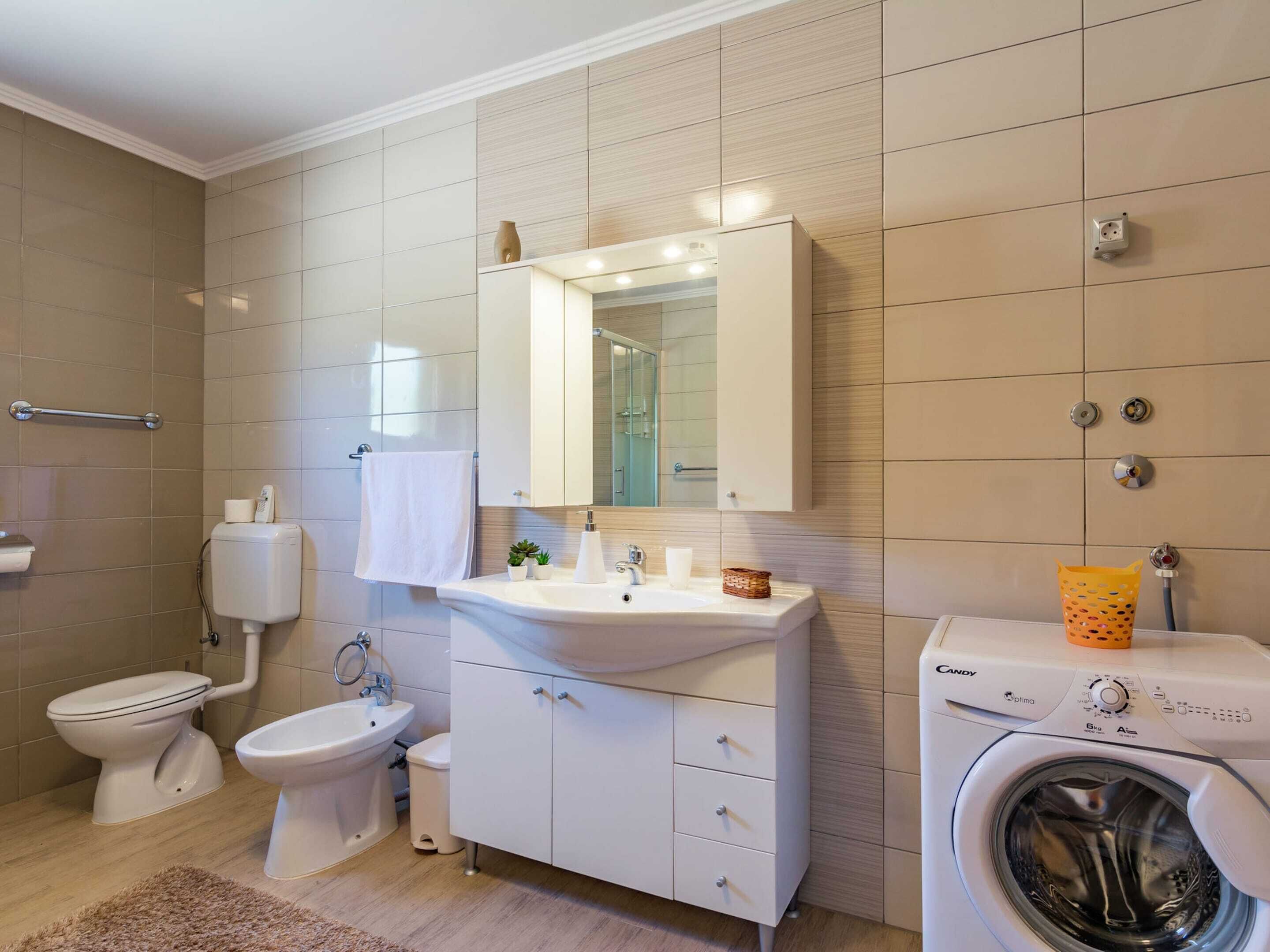 A modern bathroom with a toilet, bidet, sink, mirror, and a washing machine.