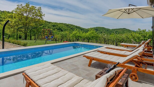 Una piscina con lettini e altalene, circondata da un giardino curato e vista sulle colline.