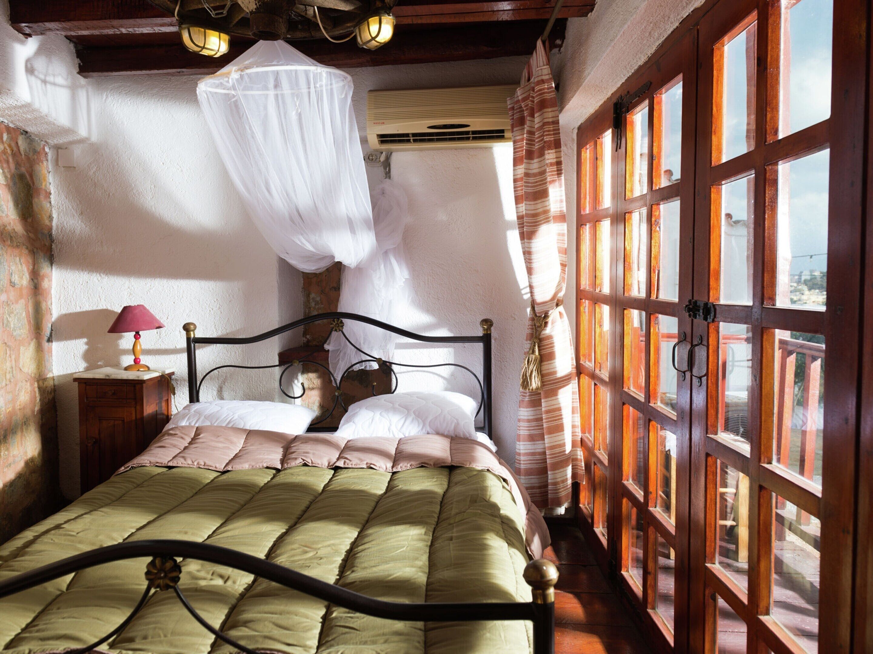 Une chambre avec un lit, une table de chevet, une fenêtre avec des rideaux et une vue sur l’extérieur.