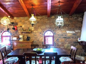 A rustic dining area with a stone wall, wooden ceiling, and hanging light fixtures. - Stone House in Elounda With Gulf Views (Agios Nikolaos)