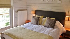 A bedroom with a bed, pillows, a headboard, a wall-mounted sign reading "HOME", a window with blinds, and a radiator. - Holiday Home in Jupille Near Forest Trails (Rendeux)