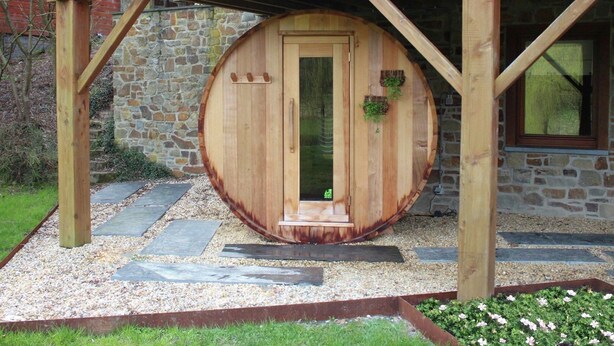 A wooden barrel-shaped door with a small step leading up to it, set in a garden with stone slabs and gravel. - Holiday Home in Jupille Near Forest Trails (Rendeux)