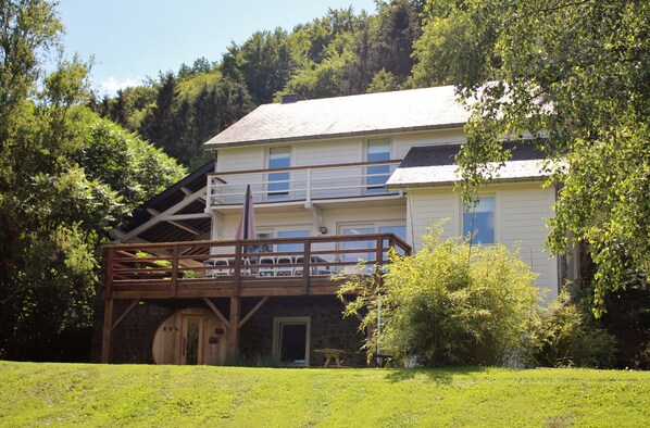 A two-story house with a wooden deck, a stone foundation, and a front door. - Holiday Home in Jupille Near Forest Trails (Rendeux)