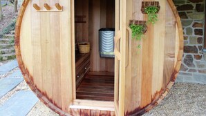 A wooden sauna with a door open, revealing a bench and a sauna heater inside. - Holiday Home in Jupille Near Forest Trails (Rendeux)
