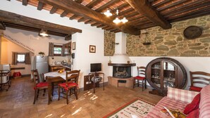 Un intérieur rustique avec des poutres apparentes, un mur en pierre, une cheminée et un coin repas agrémenté de meubles en bois.