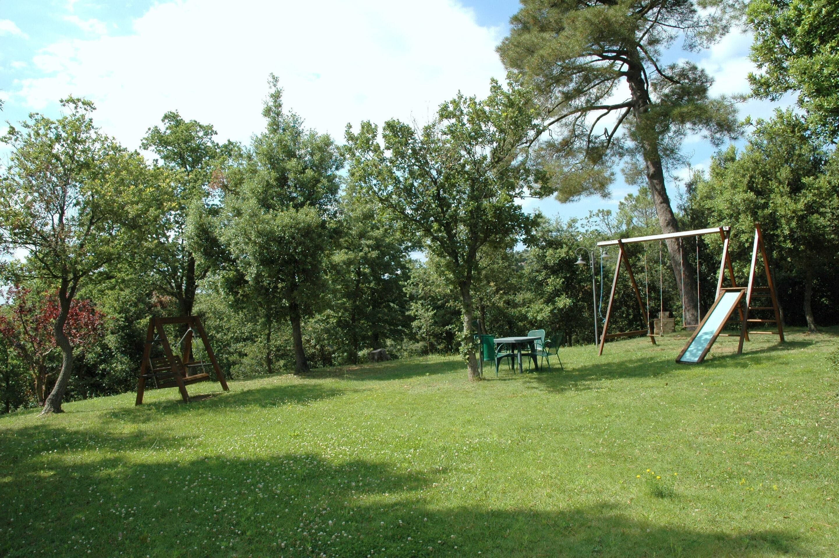 Un parque con césped, un conjunto de columpios, una mesa de picnic y bancos.