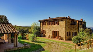 Une maison en pierre avec un toit en tuiles, un patio couvert et un chemin en pierre menant à l’entrée.