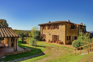 Um edifício de pedra com telhado em telhas, alpendre coberto e caminho de pedra.