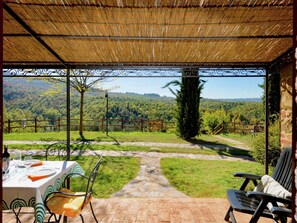 En udendørs terrasse med et spisebord, en stol og udsigt til et skovlandskab.