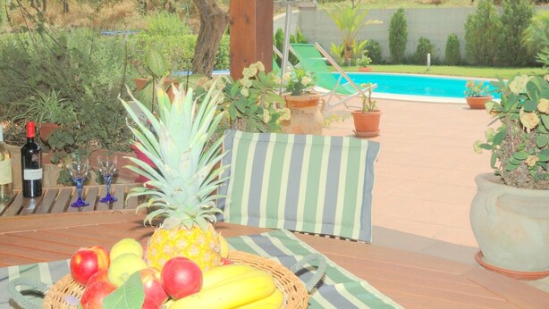 Une terrasse en bois avec une table dressée pour un repas, agrémentée d’un panier de fruits, d’une bouteille de vin et de verres.