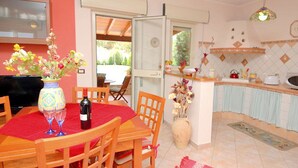 Un coin repas avec une table dressée pour deux personnes, un vase rempli de fleurs et une bouteille de vin.