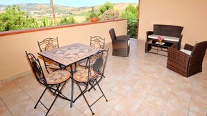 Une terrasse avec une table et des chaises, un canapé en osier et une vue sur la campagne.