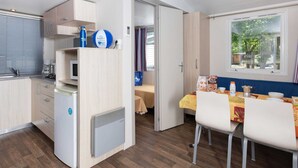 Cocina compacta con microondas, hervidor y refrigerador pequeño. Hay un comedor con mesa y sillas, y una ventana con vistas a la vegetación.