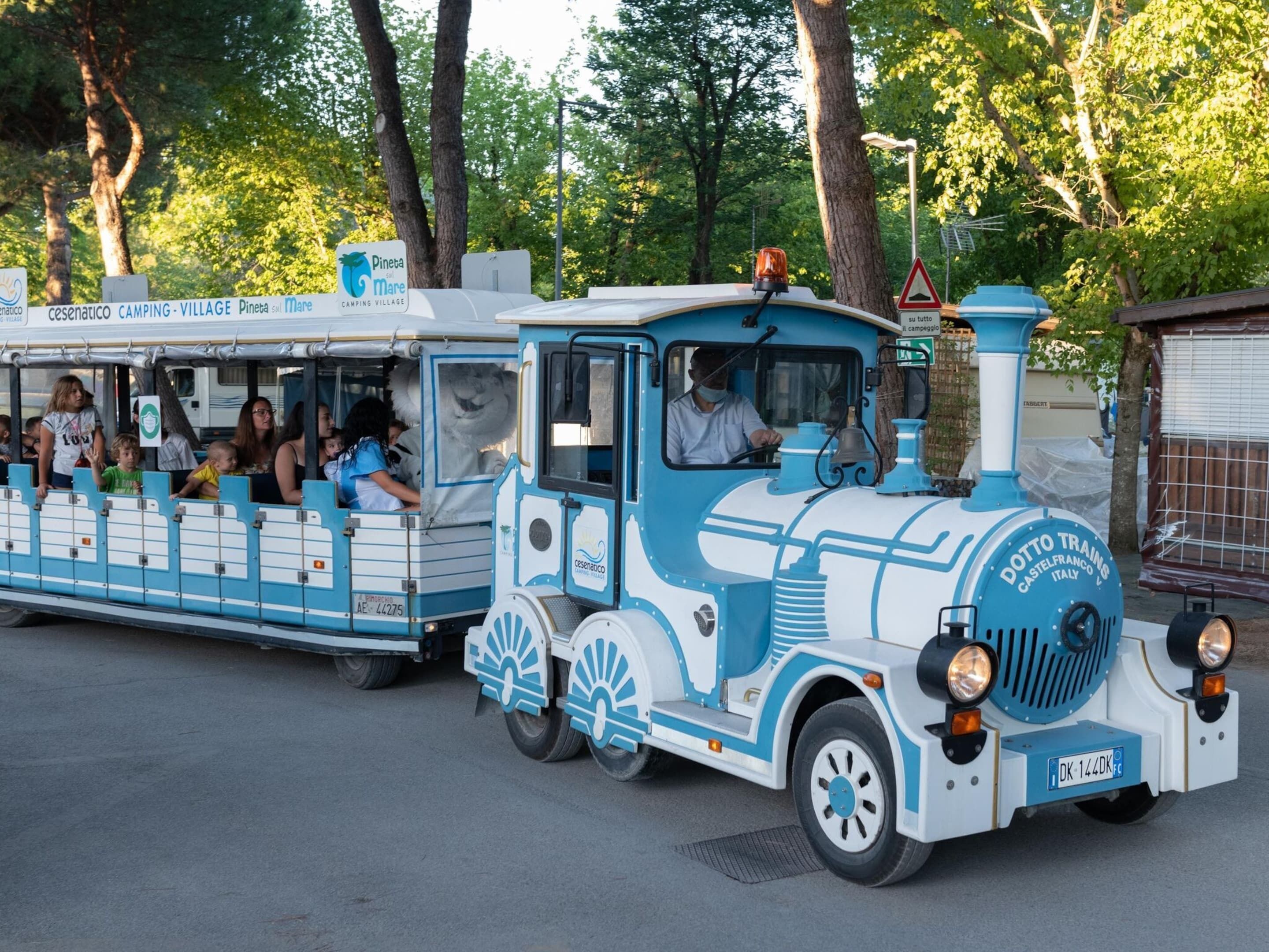 Een blauw-witte trein met passagiers, aangeduid als 'Cesenatico Camping - Village Pineta sul Mare'.